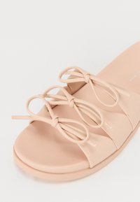 Peskefarget skyvesandal laget av glatt materiale, med tre knyttede stropper og en formet såle for komfort.