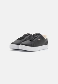 Black leather sneakers with flat white soles, lace-up front, and a beige accent at the heel. Features a small logo detail on the side.