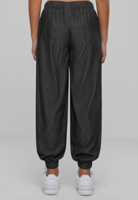 Dark gray, loose-fitting sweatpants with an elastic waistband, tapered cuffs, and smooth texture, paired with white sneakers.