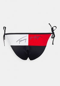 Parte inferior de biquíni em preto, vermelho e branco com laterais ajustáveis; apresenta as assinaturas "Tommy" e "Hilfiger" em cores contrastantes nos painéis. Textura suave.