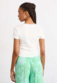 Crop top blanc à manches courtes en coton, associé à un pantalon vert fluide avec des motifs floraux légers. Encolure ronde simple.