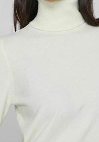 Pull à col roulé crème clair en tissu doux, doté d'une coupe ajustée et de bords côtelés au niveau du col, des poignets et de l'ourlet.