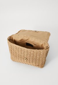 Woven straw handbag with a tan fabric interior. Features a magnetic closure and interior pockets, showcasing a rectangular shape and natural texture.