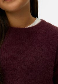 Maglione bordeaux morbido con scollo rotondo e tessuto strutturato. Sotto il colletto si intravede un strato bianco.