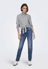 Chemise à rayures grises et blanches, boutonnée et nouée à la taille ; associée à un jean bleu à jambes droites et des baskets blanches. Design simple, style décontracté.