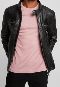 Svart skinnjacka med silverfärgade dragkedjor, med ståkrage och flera fickor med dragkedja över en rosa T-shirt. Texturerad yta.