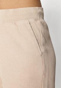 Béžové žebrované joggers s elastickým pasem, boční kapsou a měkkou texturou pro pohodlné nošení. Detailní záběr na látku a detaily.