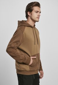 Brun hettegenser med fargeblokkdesign, kengurulomme, ribbestrikkede mansjetter og snor i hetta. Laget av myk, teksturert stoff.
