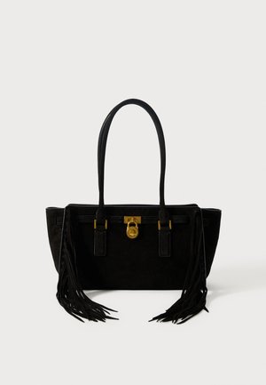 Sac en suede noir avec de longs accents de franges, accessoires en or et deux poignées robustes. Forme rectangulaire avec une texture lisse.