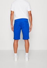 Blå shorts för män med en slät textur, bakfickor, bältesöglor och rak passform. Bärs med en vit t-shirt och vita skor.