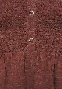 Robe couleur rouille avec smock texturé au corsage, boutons en métal argenté et jupe fluide froncée.