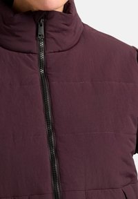 Paarse puffer gilet met hoge kraag, ritssluiting aan de voorkant en horizontaal quiltontwerp. Zachte textuur; duurzaam materiaal. Zwarte ritsdetails.