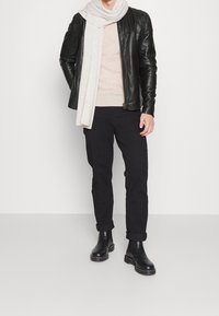 Giacca di pelle nera, maglione leggero, sciarpa grigia, pantaloni scuri arrotolati e stivali Chelsea neri. Texture morbide e palette di colori neutri.