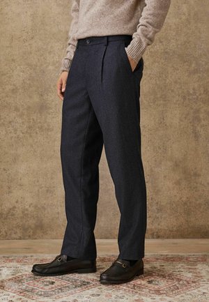 Dark blue tailored trousers with a smooth texture, featuring front pleats and side pockets, paired with black leather loafers.
