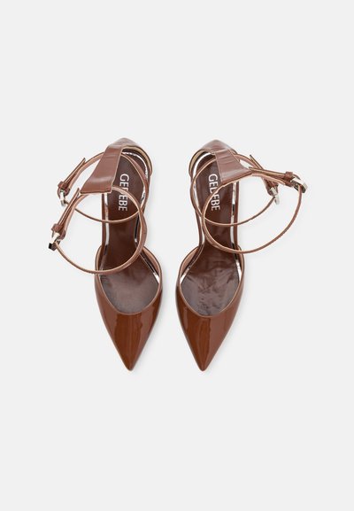 Zapatos de charol marrón de tacón alto con punta afilada, correa al tobillo y acentos metálicos en la parte superior. Textura suave y brillante.