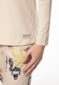 Beige overhemd met lange mouwen van zachte stof, voorzien van een waslabel. De broek heeft een multicolore abstracte print in aardetinten en speelse ontwerpen.