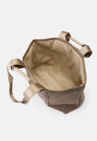 Torba tote w brązowym materiale z beżowym wnętrzem. Posiada grube beżowe uchwyty, otwarte dno i brak zapięcia. Prosty, nieozdobiony design.