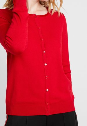 Cardigan en tricot rouge avec des manches longues, un col rond et une fermeture à boutons sur le devant. Texture lisse avec des boutons en métal argenté.