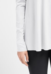 Langærmet, lysegrå top med en glat, blød tekstur og en let drapering. Kombineret med sorte, tætsiddende leggings, der fremhæver en elegant silhuet.