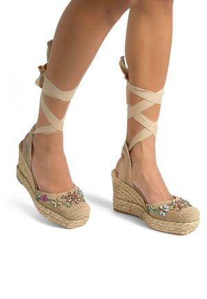 Sandali con zeppa in espadrille beige, suola in juta intrecciata, lacci alla caviglia e decorazioni floreali colorate sulla parte anteriore.