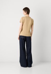 Tan kortemouwen T-shirt en donkere wijde jeans, met een gladde textuur en eenvoudig ontwerp, gezien vanaf de achterkant.