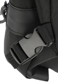 Dettaglio di una borsa in nylon nera con superficie testurizzata, una fibbia a clip in plastica e un attacco per la tracolla resistente.