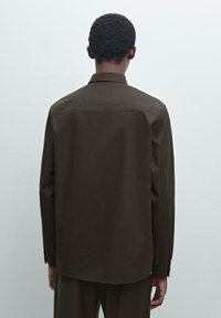 Brown long-sleeve shirt in a smooth fabric, featuring a straight back, buttoned cuffs, and a classic collar. Tailored fit with a curved hem.
