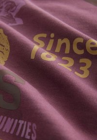 Tissu bordeaux au toucher lisse, avec du texte doré et violet clair, incluant "depuis 1823" et "opportunités."