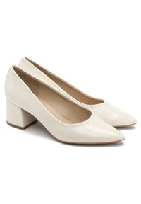 Białe lakierowane szpilki na wysokim obcasie z ostro zakończonym noskiem i słupkowym obcasem, o gładkiej fakturze i minimalnym wykończeniu.