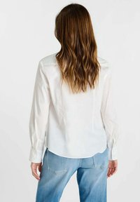 Witte shirt met lange mouwen, een gladde, lichtgewicht textuur en een afgeronde zoom. Gecombineerd met lichtblauwe spijkerbroek, wat een casual stijl laat zien.