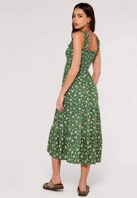 Grünes Blumenkleid mit Rüschenträgern, einem taillierten Oberteil und einem gestuften Rock. Der Stoff hat eine weiche Textur mit kleinen, hellen Blumen.