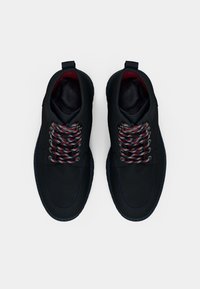 Botas de tobillo negras con cordones presentan un exterior suave, un forro rojo contrastante y suelas texturizadas.