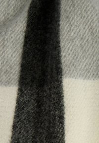 Tessuto morbido e peloso con ampie strisce verticali in nero, grigio chiaro e bianco sporco, che mostrano un motivo di maglia testurizzato.