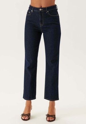 Höga mörkblå jeans med rak bendesign, guldstickningar och stängning framtill med knapp. Texturerat denimtyg.