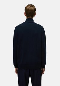 Maglione a collo alto di colore blu navy, con polsini e orlo a coste, e una finitura testurizzata. La vista posteriore mostra una vestibilità rilassata e un tessuto morbido.