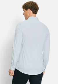 Langarmhemd aus hellblauem Stoff mit einem subtilen geometrischen Muster. Klassischer Kragen und Knopfmanschetten, mit abgerundetem Saum.