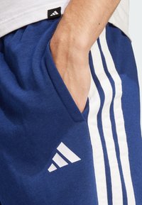 Blå sportshorts i bomull med vita vertikala ränder och en logodetalj. Inkluderar sidofickor och resårmidja.