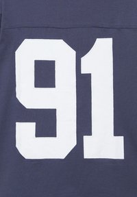 Numéro blanc "91" imprimé sur un tissu bleu foncé, probablement une partie d'un maillot de sport ou d'un sweat.