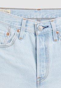 Světlé modré džínové kalhoty s knoflíkovým zapínáním, měděnými nýty a oranžovým prošíváním. Tkanina má vybledlou strukturu a klasický design s pěti kapsami.