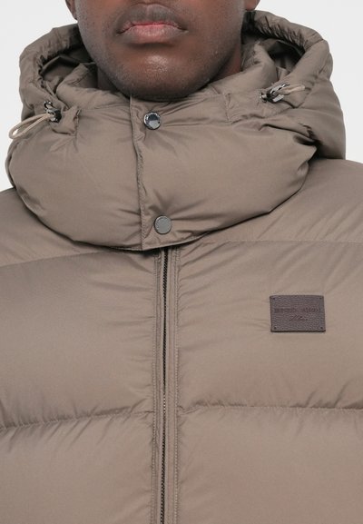 Puffer jacket in taupe with a quilted pattern, high collar hood, front zipper, and a leather brand accent above the zipper.