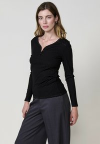 Haut noir à manches longues côtelé avec un patte de boutonnage semi-ouverte et une coupe slim. Associé à un pantalon large gris, il met en valeur une silhouette élégante.