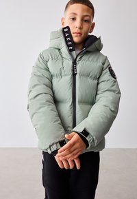 Geacă puffer verde cu glugă, cu fermoar frontal, accente negre, etichetă a mărcii pe gât și manșete elastice.