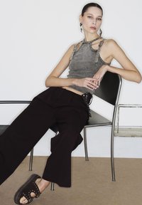 Top a righe grigio con design unico dei spallini, abbinato a pantaloni neri larghi, indossato con sandali scuri con borchie su una sedia.