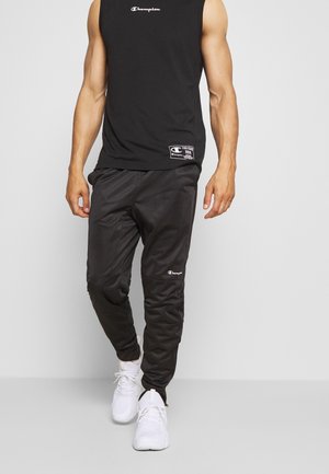 Zwarte sportieve broek met een gladde textuur, met een Champion-logo. Gecombineerd met een zwarte mouwloze top en witte sneakers.