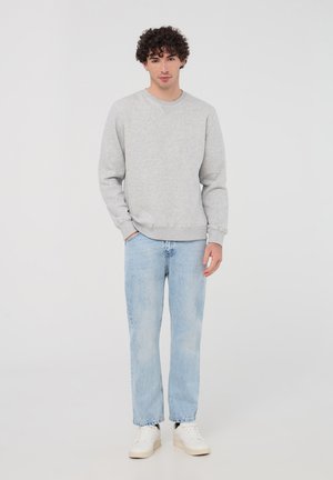 Szary sweter z żeberkowymi mankietami i dołem, zestawiony z jasnoniebieskimi prostymi dżinsami i białymi trampkami. Gładki, bez widocznych wzorów.