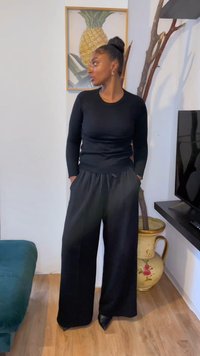 Črni dolgi rokavi v kombinaciji z visokim pasom in širokimi črnimi hlačami. Material se zdi mehak, z ohlapnim krojem in stranskimi žepi.