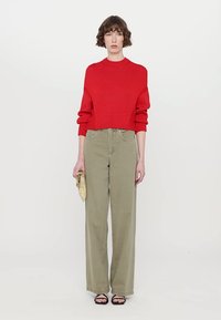Red knitted cropped sweater with ribbed texture, paired with high-waisted olive green wide-leg trousers. Black heeled sandals and a gold clutch.