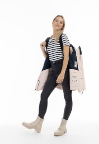 Jachetă puf light pink cu accente bleumarin, cămașă cu dungi, blugi skinny negri și bocanci bej cu șiret. Rucsac purtat pe umăr.