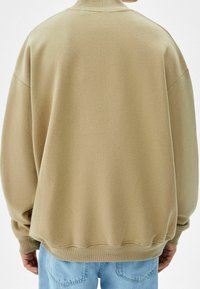 Beige oversized sweatshirt med rundad halsringning, ribbade ärmslut och nederkant. Mjuk textur, avslappnad passform. Bärs med ljusblå jeans.