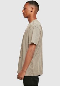 Khaki ülemäärane t-särk, mis on valmistatud puuvillast, ümmarguse kaela ja lühikeste varrukatega; esiküljel on must graafiline tekst.